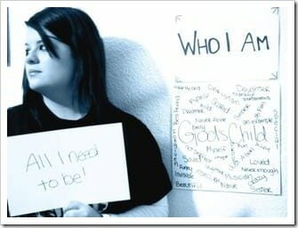 Teenage girl in front of sign saying "Who I Am" and holding a sign saying "All I need to be!"